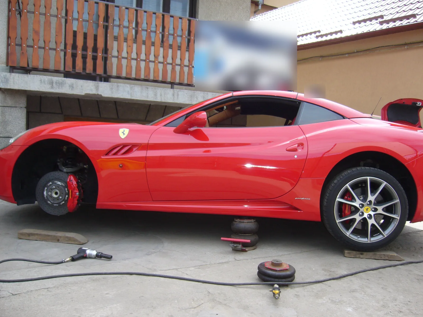 Ferrari California roșu cu roata din față demontată, în curtea atelierului
