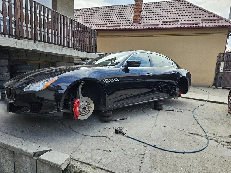 Maserati Quattroporte negru cu roata din față demontată, în curtea atelierului