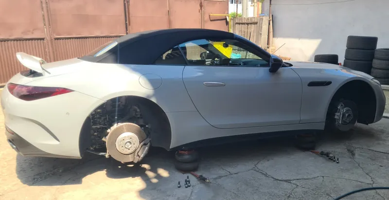 Mercedes-AMG SL decapotabil alb, din profil, cu ambele roți de pe partea dreaptă demontate