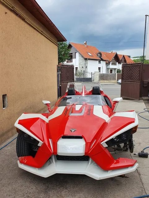 Polaris Slingshot roșu cu alb, văzut din față, în curtea atelierului