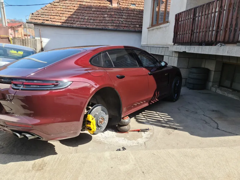 Porsche Panamera vișiniu cu roata din spate demontată, în curtea atelierului